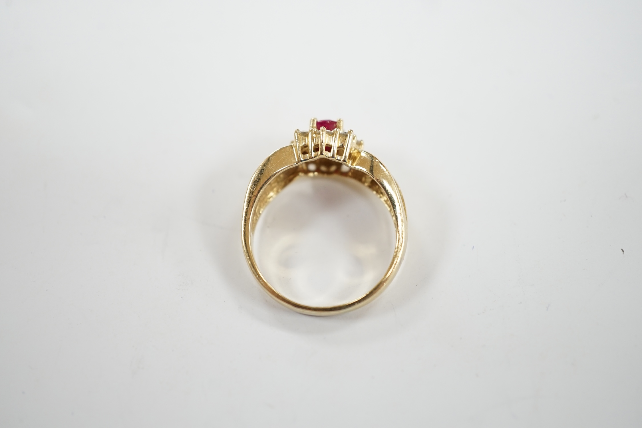 A modern 14k, ruby and diamond set oval cluster dress ring, with diamond chip set shoulders, size P, gross weight 5.1 grams.